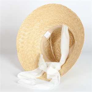 Detail of handwoven beige straw hat featuring elegant white chiffon ribbon and sweatband