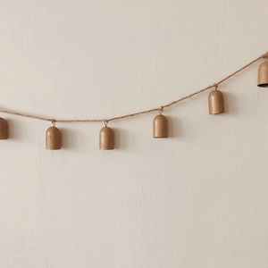 Vintage bronze metal bells on jute rope hanging against a minimalist beige textured wall