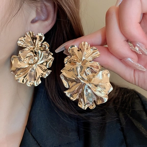 Detail of oversized gold floral earrings with textured metallic petals on model