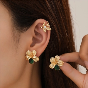 Detail of gold floral earrings set with green teardrop gems and white stone ear cuff