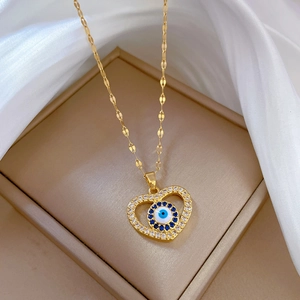 Gold heart necklace with evil eye pendant and blue crystals on a beige jewelry box