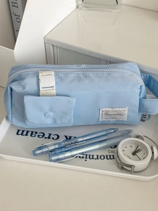 Close-up of light blue cotton-padded pencil case with front pocket and brand label