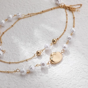 Elegant 14K gold layered necklace featuring white faux pearls and golden bean charms