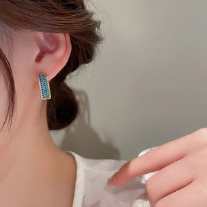 Close-up of elegant C-shaped gold earrings with blue and green pave crystals on model
