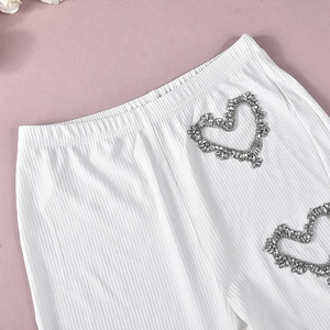 Dettaglio di pantaloni in maglia a coste bianchi con decorazione a cuore in strass lucenti