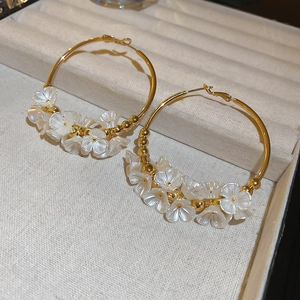Detail of gold hoop earrings featuring elegant white acrylic flowers and metallic beads