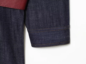 Detail of dark blue denim sleeve with yellow stitching and leather patchwork accents