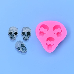 Pink 3-cavity skull silicone mold with detailed grey resin skull figurines on blue backdrop