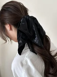 Close-up of a glossy black oversized bow hair tie worn on a high ponytail for women