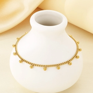 Minimalist gold beaded anklet with steel charms on white vase and beige silk