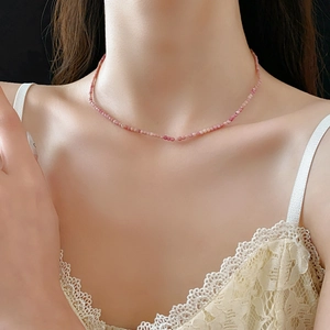 Gros plan du collier bohème en perles roses porté par un mannequin sur fond noir élégant