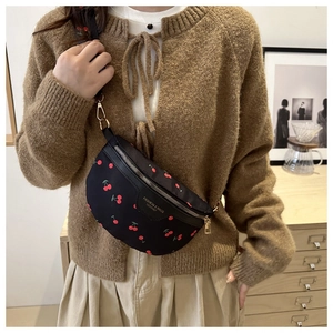 Close-up of black crossbody fanny pack with red cherry print and golden hardware detail