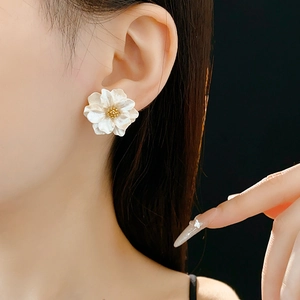 Detailed close-up of cream resin flower earrings with gold center on a model's ear