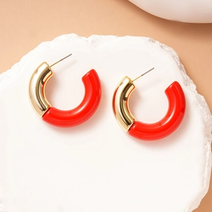 Detail of red and gold C-shaped acrylic earrings on a minimalist white stone pedestal