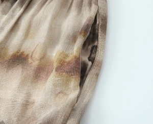Detailed view of silk-like fabric with brown tie-dye print, waist pleats and side pocket