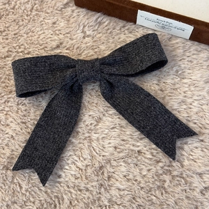 Detail of dark grey knitted bow hair clip on a soft textured cream background