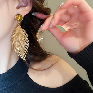 Detailed view of vintage gold feather earring with brown tiger eye stone on model ear