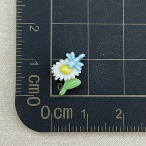Detailed macro view of a 1.2cm resin daisy and dragonfly charm on a CM scale grid