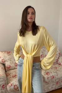 Dettaglio top in maglia gialla con nodo in vita e nastri lunghi dallo stile contemporaneo