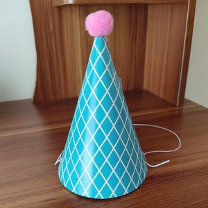 Detail of sky blue cone birthday hat with white diamond pattern and pink pompom top