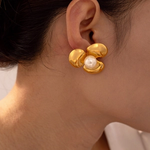 Macro detail of gold textured flower stud earring featuring a white lustrous pearl
