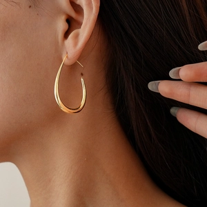 Close-up of a minimalist golden teardrop earring with a polished metallic finish on a model