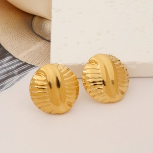 Macro shot of gold round earrings with radial texture on a white textured background