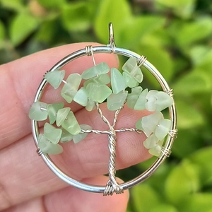 Detailed close-up of a silver wire-wrapped Tree of Life pendant with green gemstones