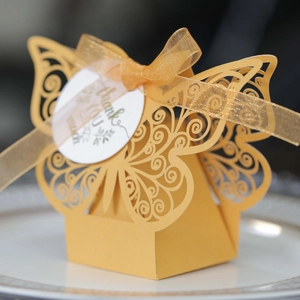 Macro shot of yellow laser-cut butterfly candy box with gold ribbon and thank you tag