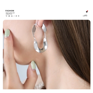 Close-up of model wearing silver twisted oval hoop earrings in polished steel finish