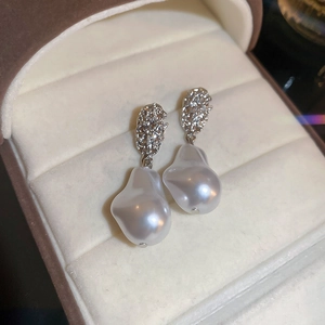 Detail of baroque pearl drop earrings with irregular silver metal texture on velvet tray