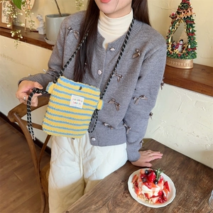 Détail du sac bandoulière en peluche rayée avec sangle tissée dans un café chaleureux