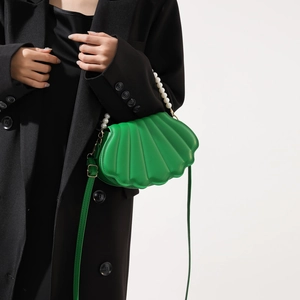 Detail of green shell-shaped crossbody bag with pearl handle worn by model in black blazer