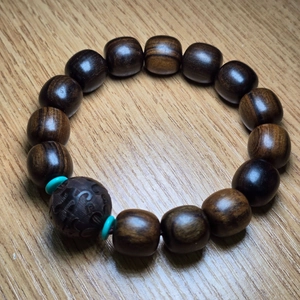 Gros plan de perles de prière en bois d'agar brun avec séparateurs turquoise et gravure