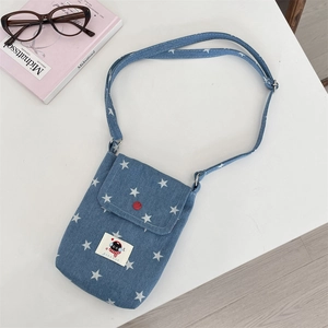 Detail van blauwe denim schoudertas met sterren, rode knoop en cartoon kattenpatch