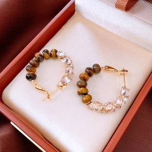 Close-up of golden hoop earrings featuring brown tiger eye beads and zircon in a jewelry box
