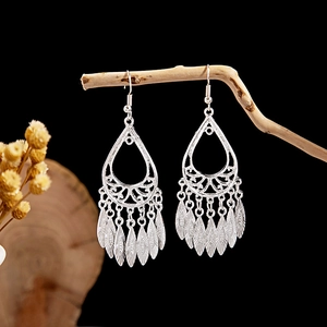 Detailed view of silver ethnic leaf tassel earrings hanging on a natural wooden branch