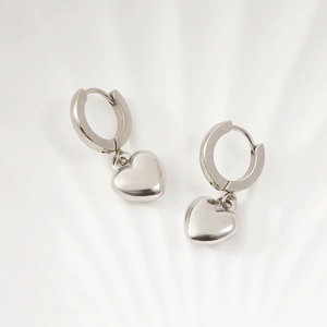 Detail shot of silver heart pendant earrings with smooth metallic finish on white surface