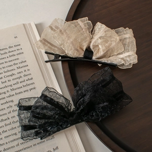 Elegant organza bow hair clips in beige and black displayed on a wooden tray with books
