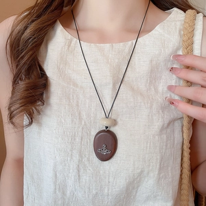 Close-up of a vintage wood oval pendant featuring a silver orb emblem on a linen background