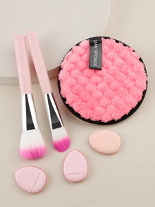 Pink makeup tool set featuring brushes, soft powder puffs and beauty sponges on stone display