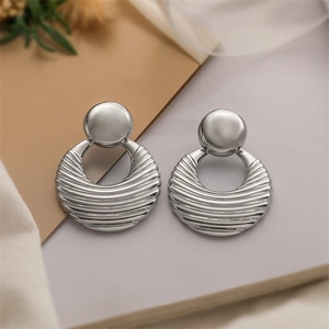 Detailed view of silver metallic bow earrings with ripple texture on elegant neutral background