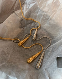 Macro shot of gold and silver teardrop pendants on snake chains inside white packaging