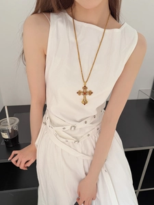 Détail du pendentif croix dorée vintage avec strass rouges porté par un mannequin