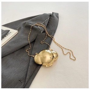 Detail of a golden metal shell-shaped evening bag with a chain strap on a textured cloth