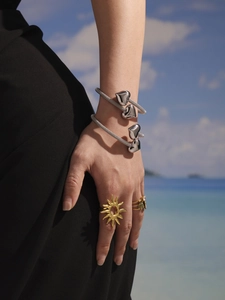 Close-up of heart-shaped silver bangles and golden sun ring worn on a beach background