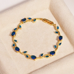 Makroaufnahme des goldfarbenen Rankenarmbands mit tiefblauen Zirkonia in einer Box