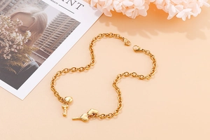 Detailed close-up of golden stainless steel bracelet with heart and key charms on warm backdrop