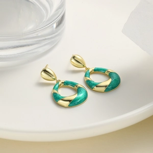 Close-up of golden oval textured earrings with emerald green enamel on a ceramic tray