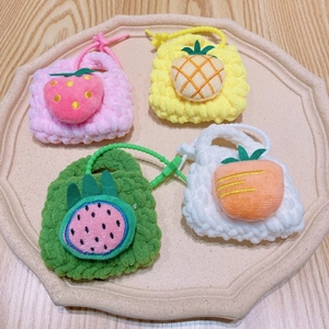 Mini hand-knitted fruit purses including strawberry and pineapple on a ceramic plate